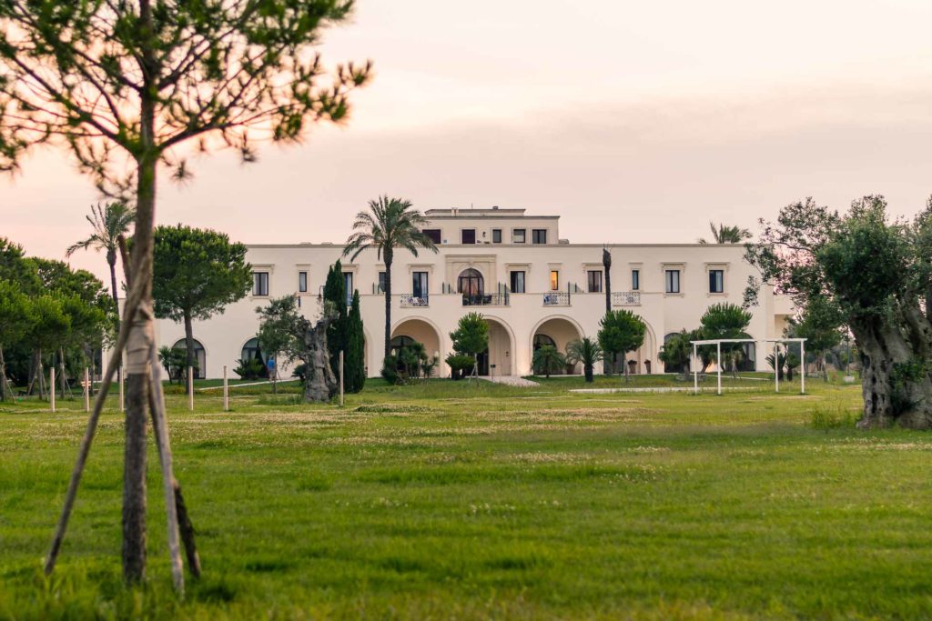 Uma casa muito grande ao fundo, sede da masseria Tenuta La Baronessa, em meio ao campo verde