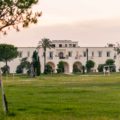 Uma casa muito grande ao fundo, sede da masseria Tenuta La Baronessa, em meio ao campo verde