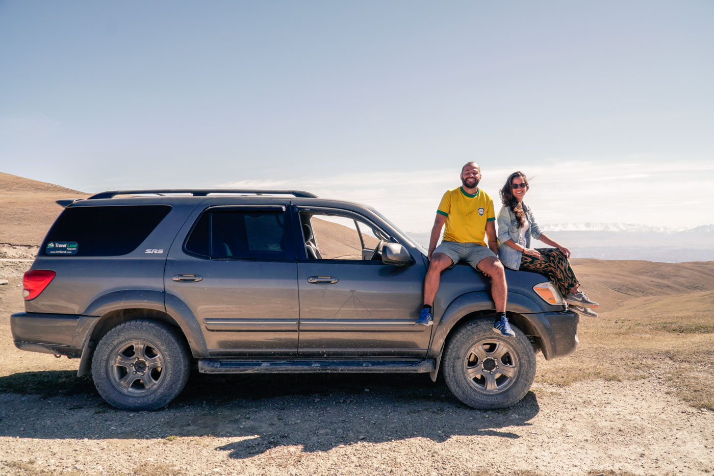 Tiago and Fernanda sitting on top of the car in the middle of nowhere in Kyrgyzstan