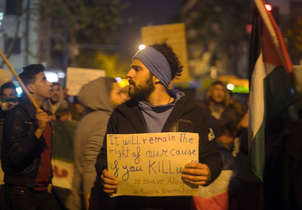 Um Sírio segurando um cartaz dizendo: Vai continuar sendo nossa causa justa, mesmo que continuem nos matando