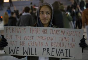 Refugiado Sírio segurando um cartaz dizendo: "Talvez haja lágrimas na vida real, mas a coisa mais importante é que criamos uma revolução. Nós prevaleceremos"