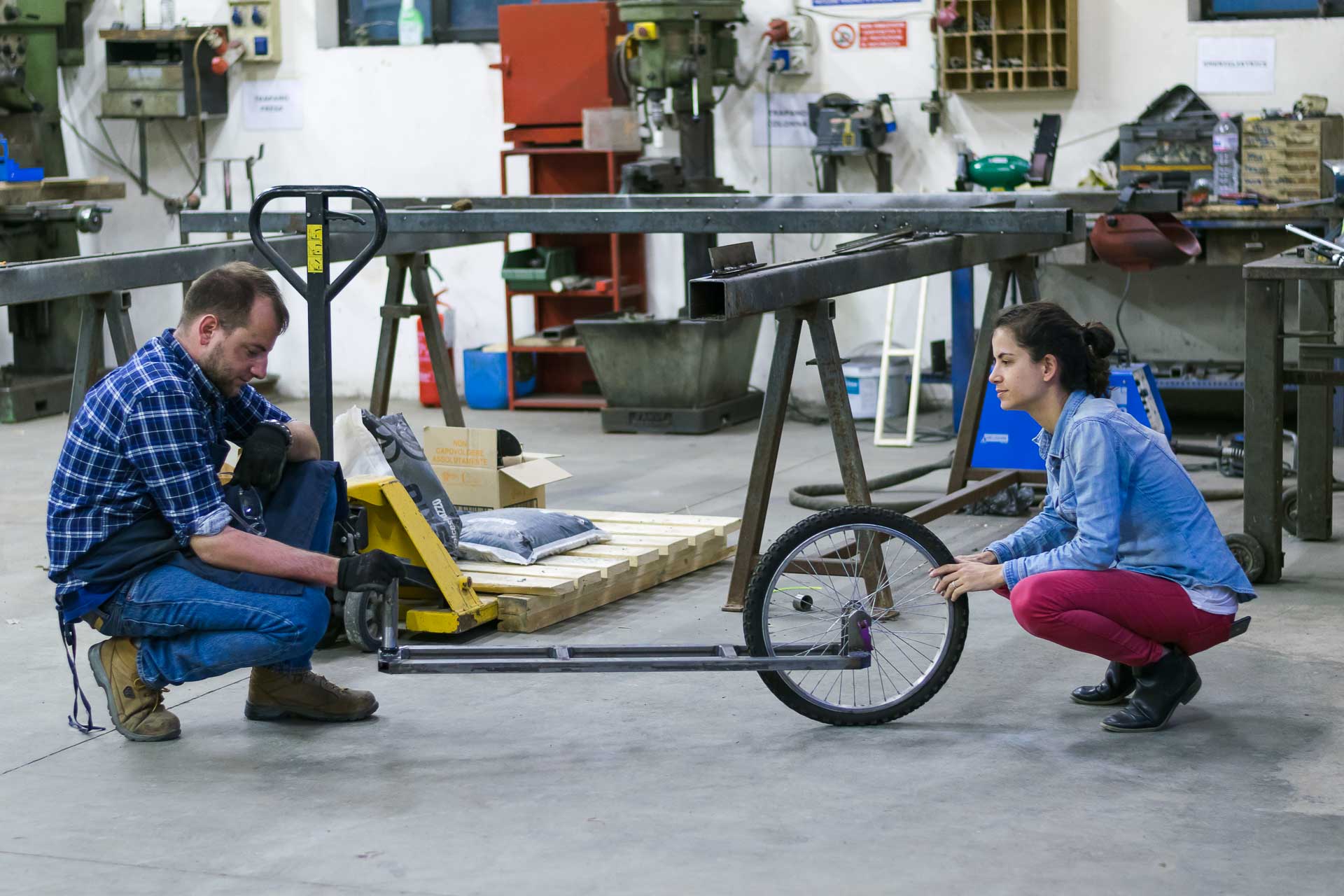 Fernanda and the bike mechanic in a shop squatting checking the bike trolley manual made