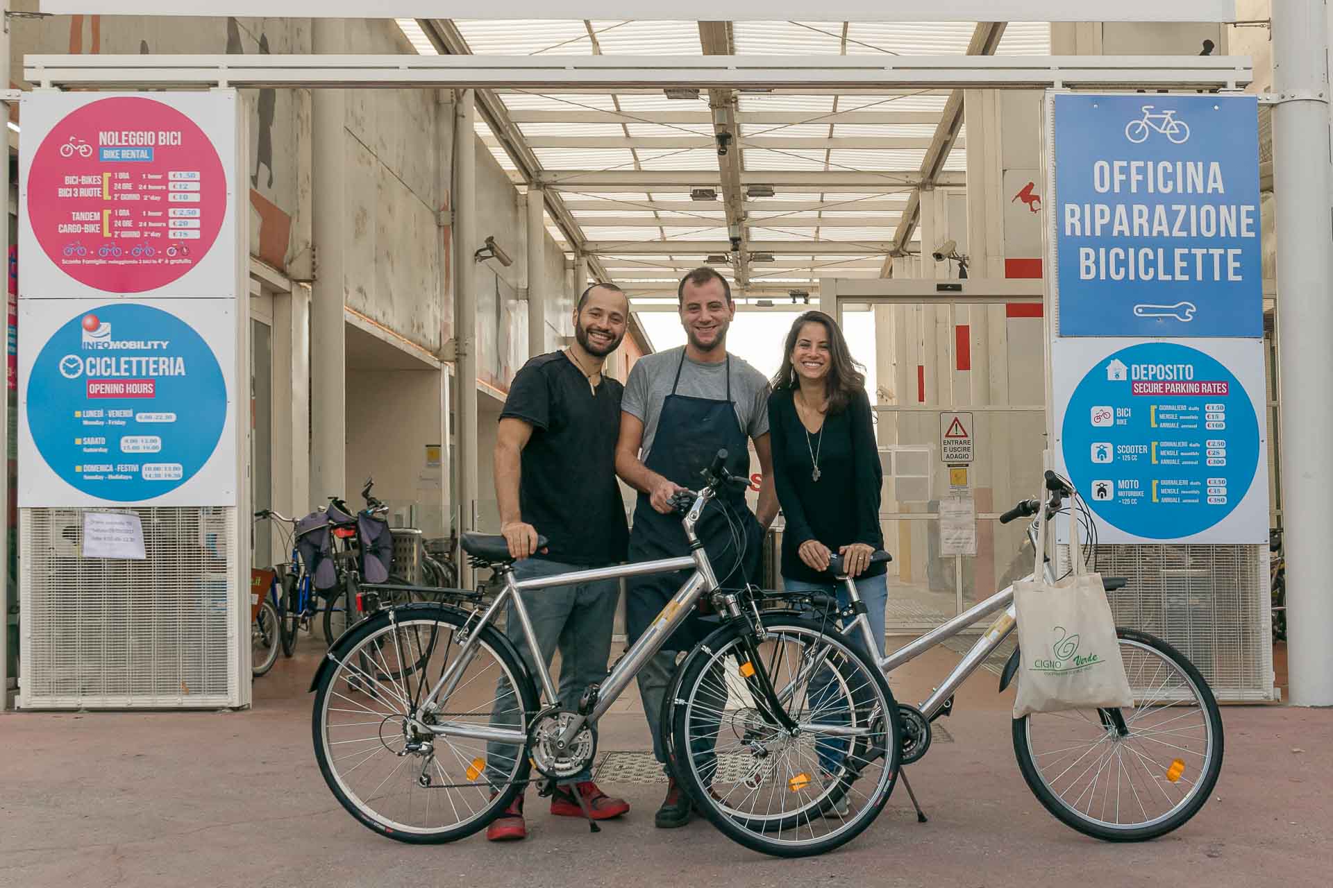 Tiago and Fernanda in front of the bike shop with two bikes and the bike mechanic