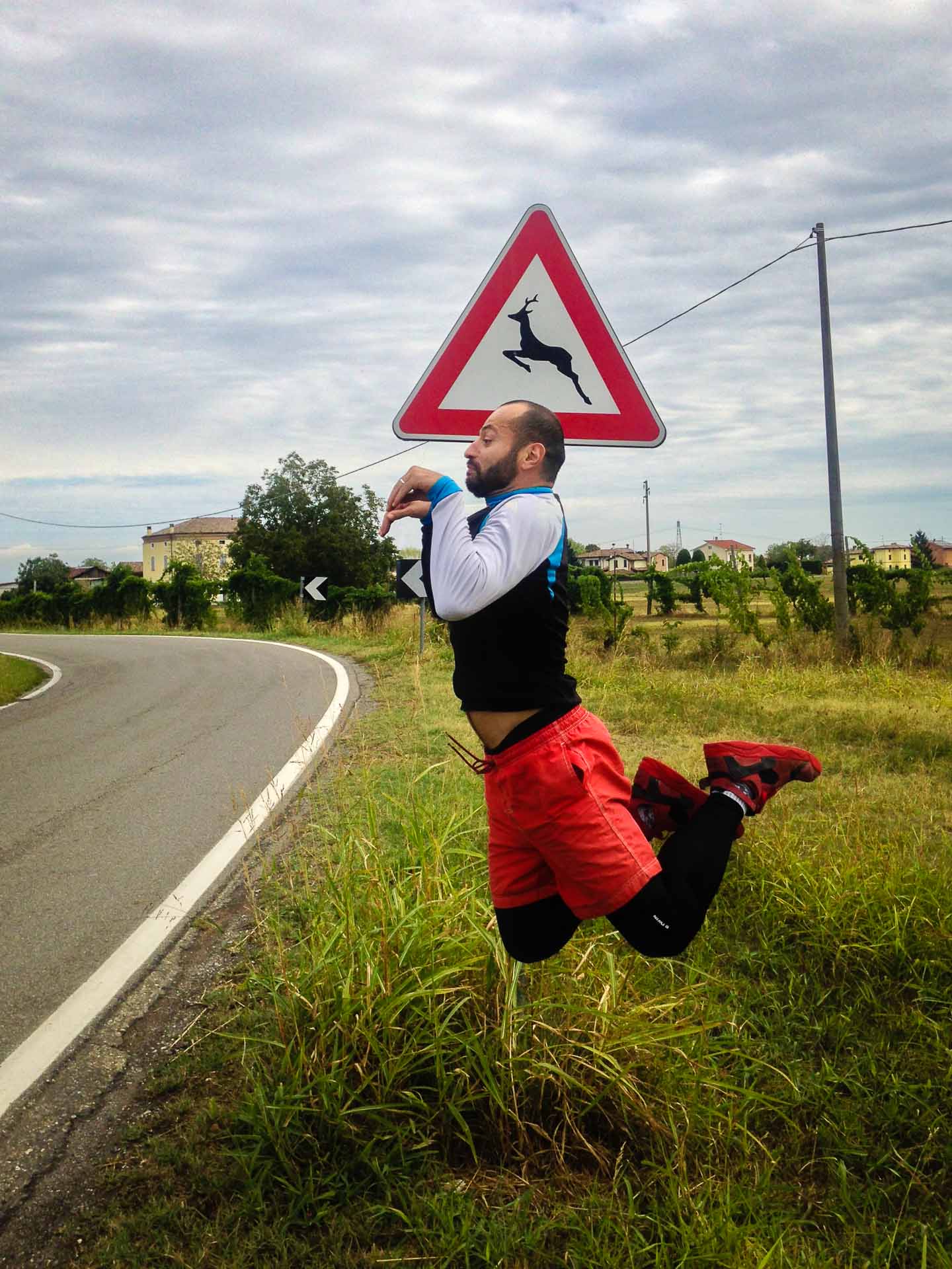 Tiago jumping like a deer in front of a road sign that shows a deer jumping