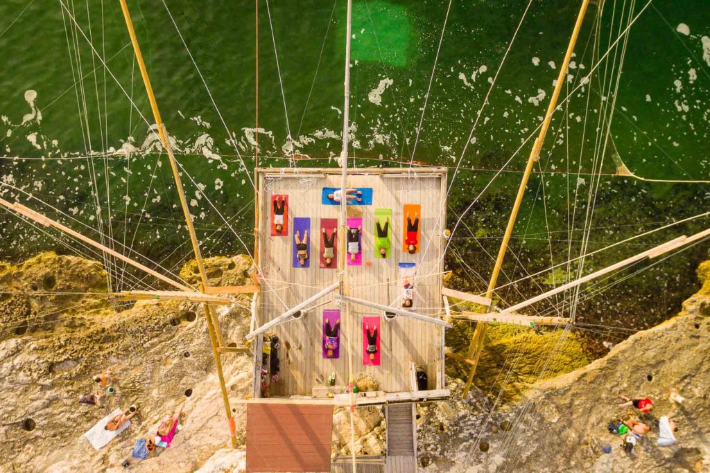 A overhead shot of people doing yoga on a trabucco by the coast, an activity perfect for your Puglia itinerary