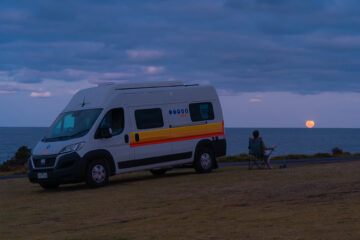 Fernanda sitting on a chair in front of a motorhome watching the full moon on the horizon in Australia