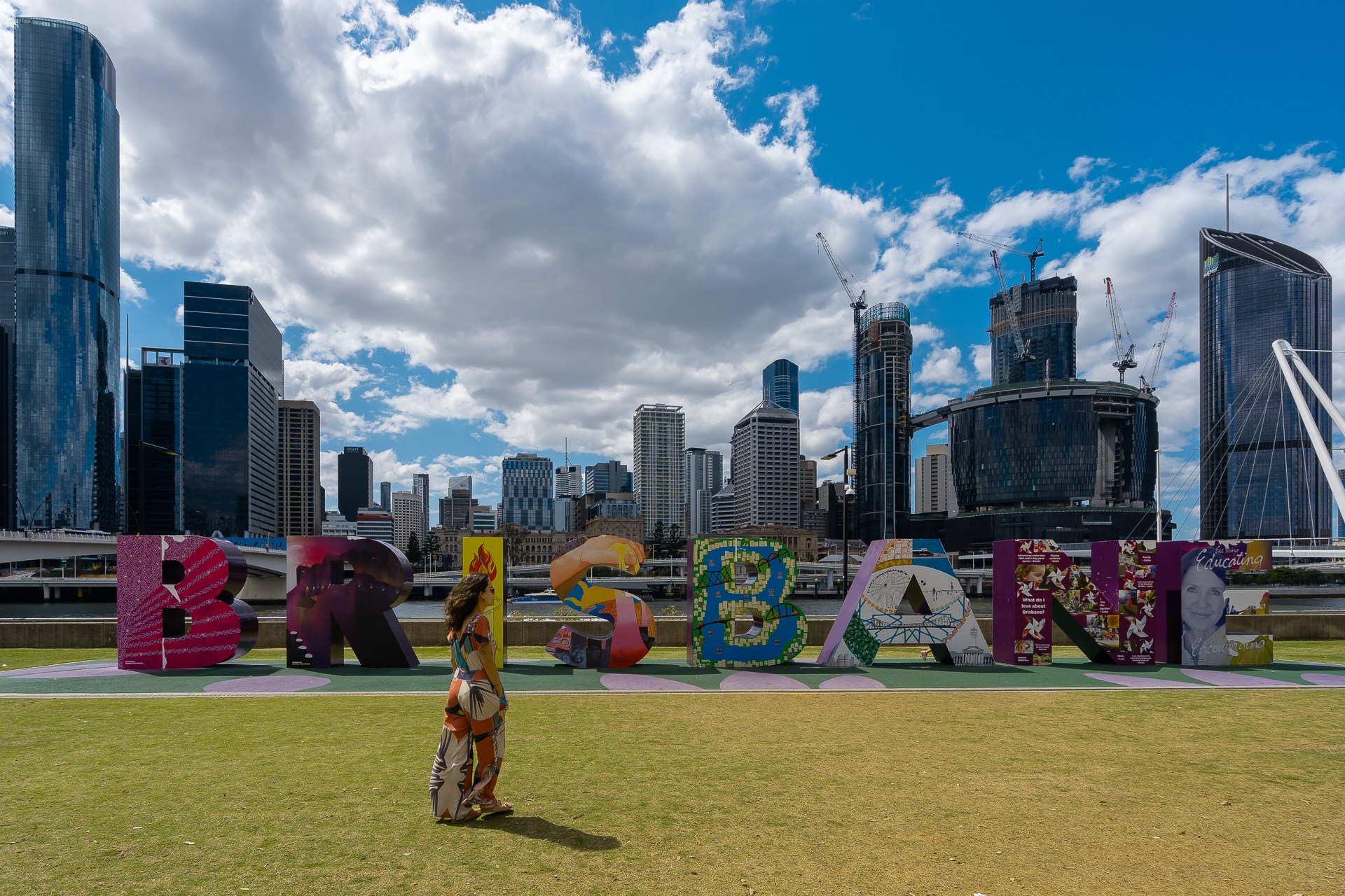 Fernanda in front of a sign saying Brisbane during our road trip in Australia with buildings in the background