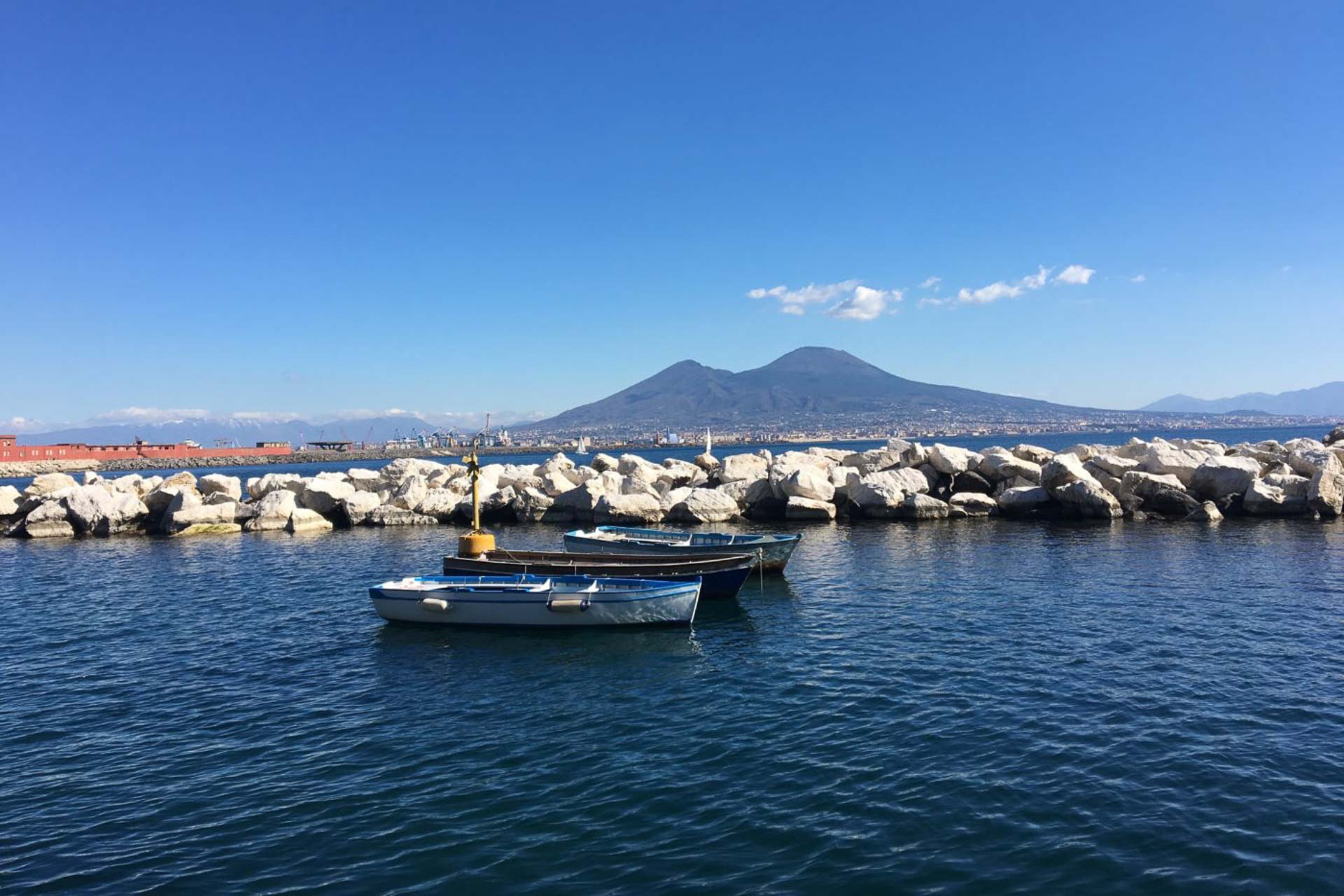 Um barco parado perto das pedras na orla de Nápoles com uma montanha ao fundo
