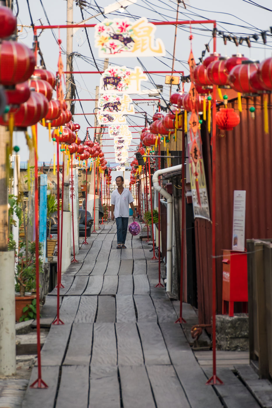 Um Chinês andando em uma plataforma de madeira que conecta as casas de palafita em Pegang