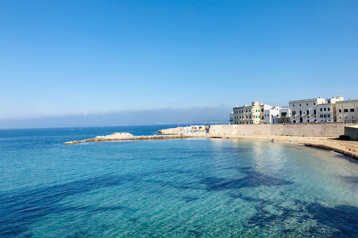 Uma praia de pouca areia com uma agua azul clara na Puglia