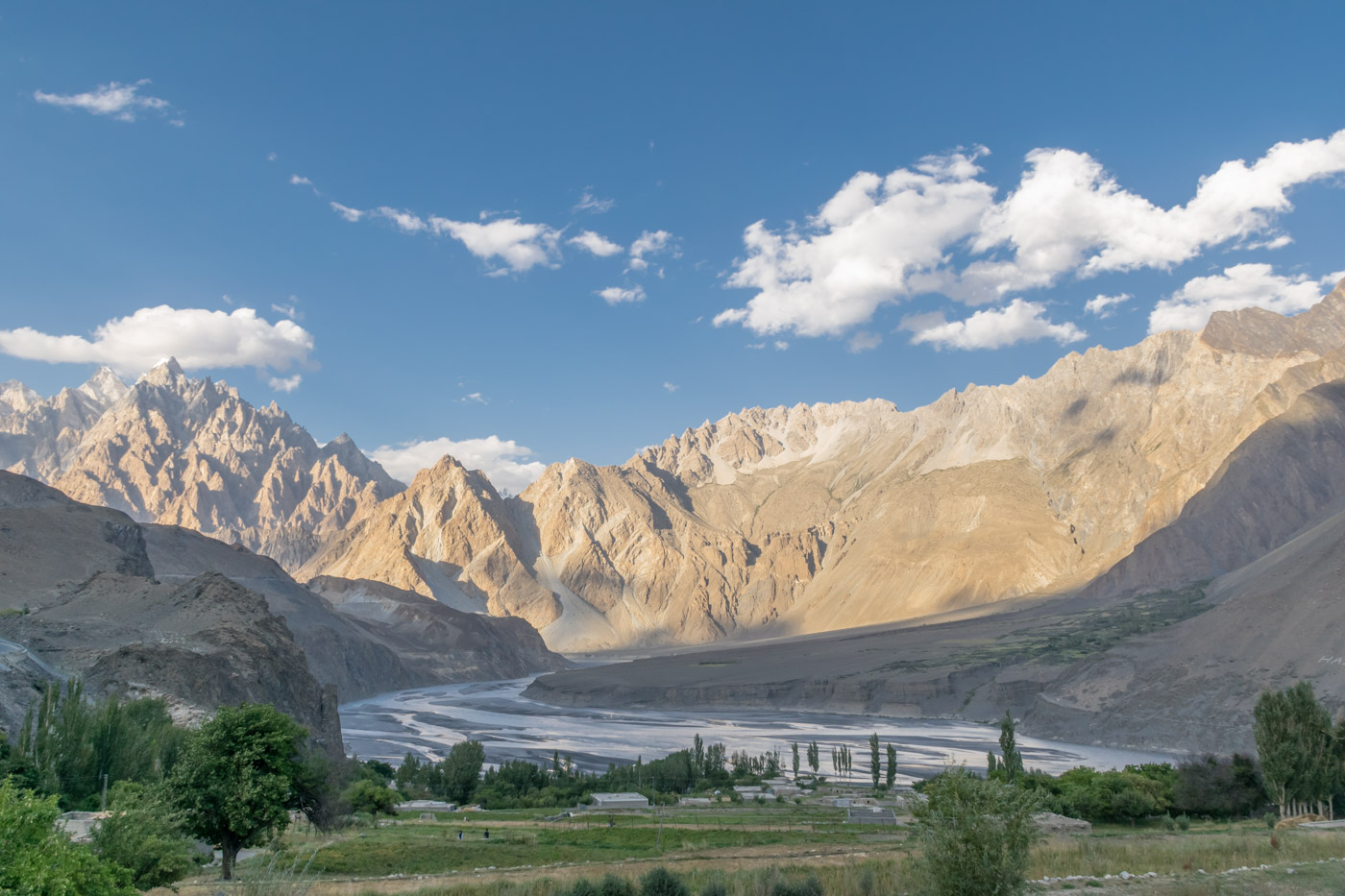 A large chain of mountains illuminated by the son with a river coming out from it in Hunza Valley