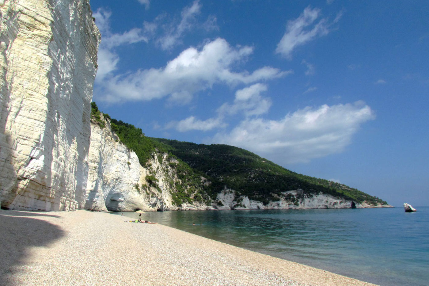 Praia rente a uma colina branca enorme, com pouca areia