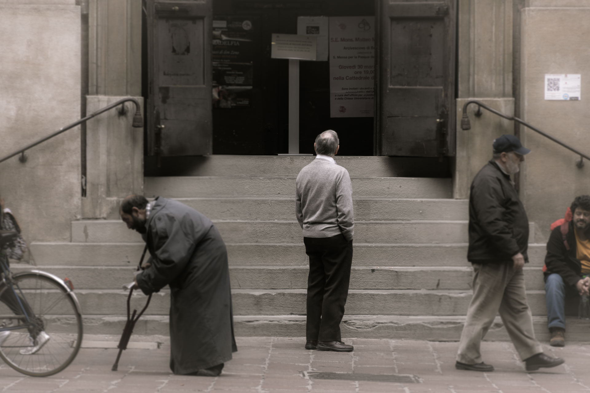 Um senhor bem corcunda passando na frente da igreja de Bologna na Italia enquanto um homem olha para a porta da igreja