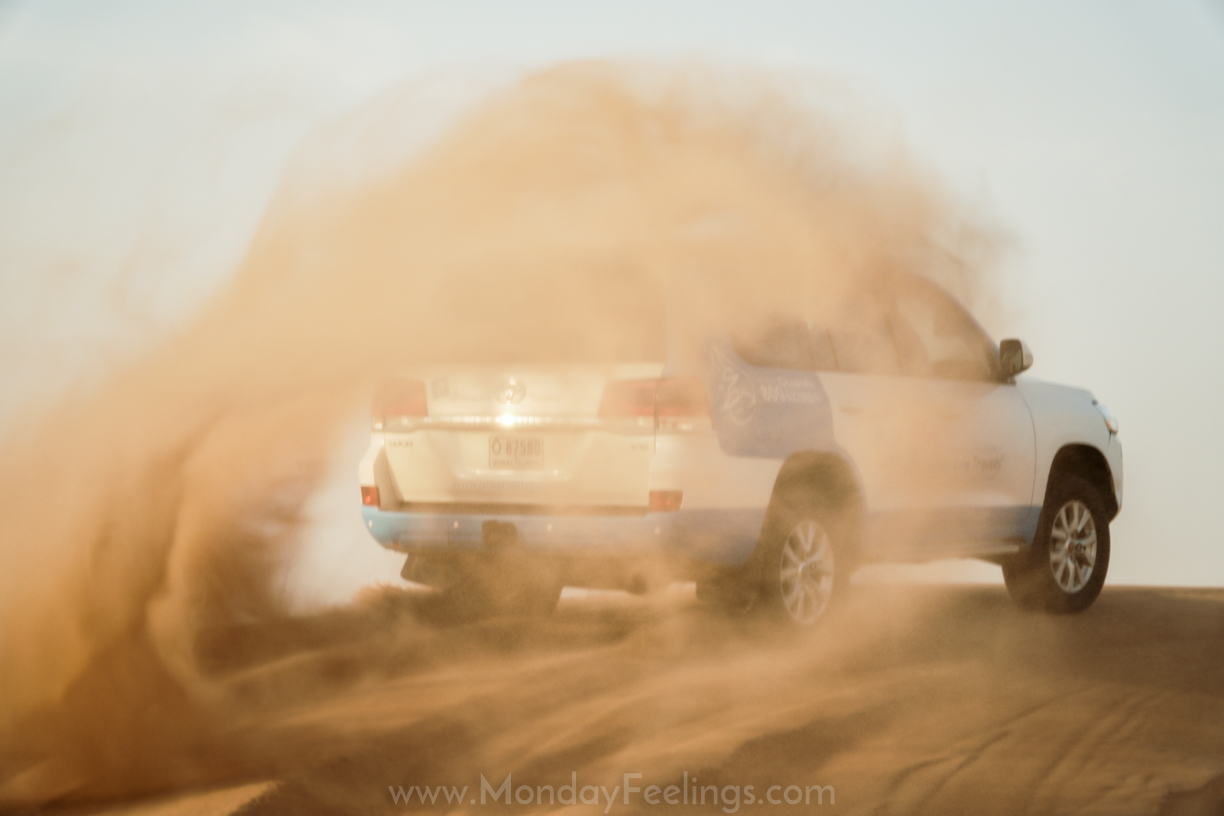 a car making the sand of the dunes go to air while driving in the dunes of Dubai