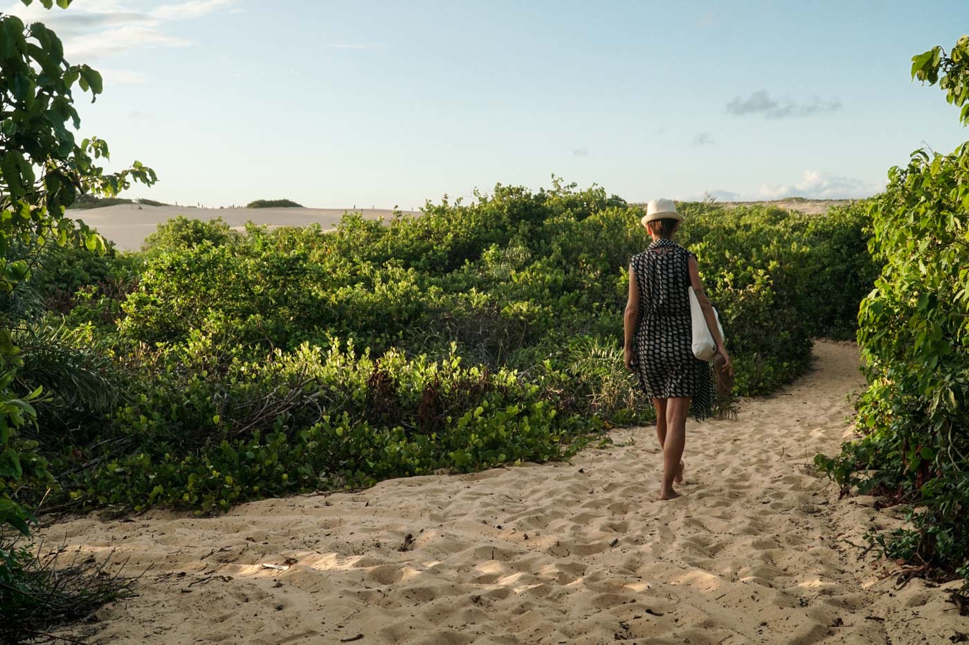 Fe walking in the sand surrounded by vegetation