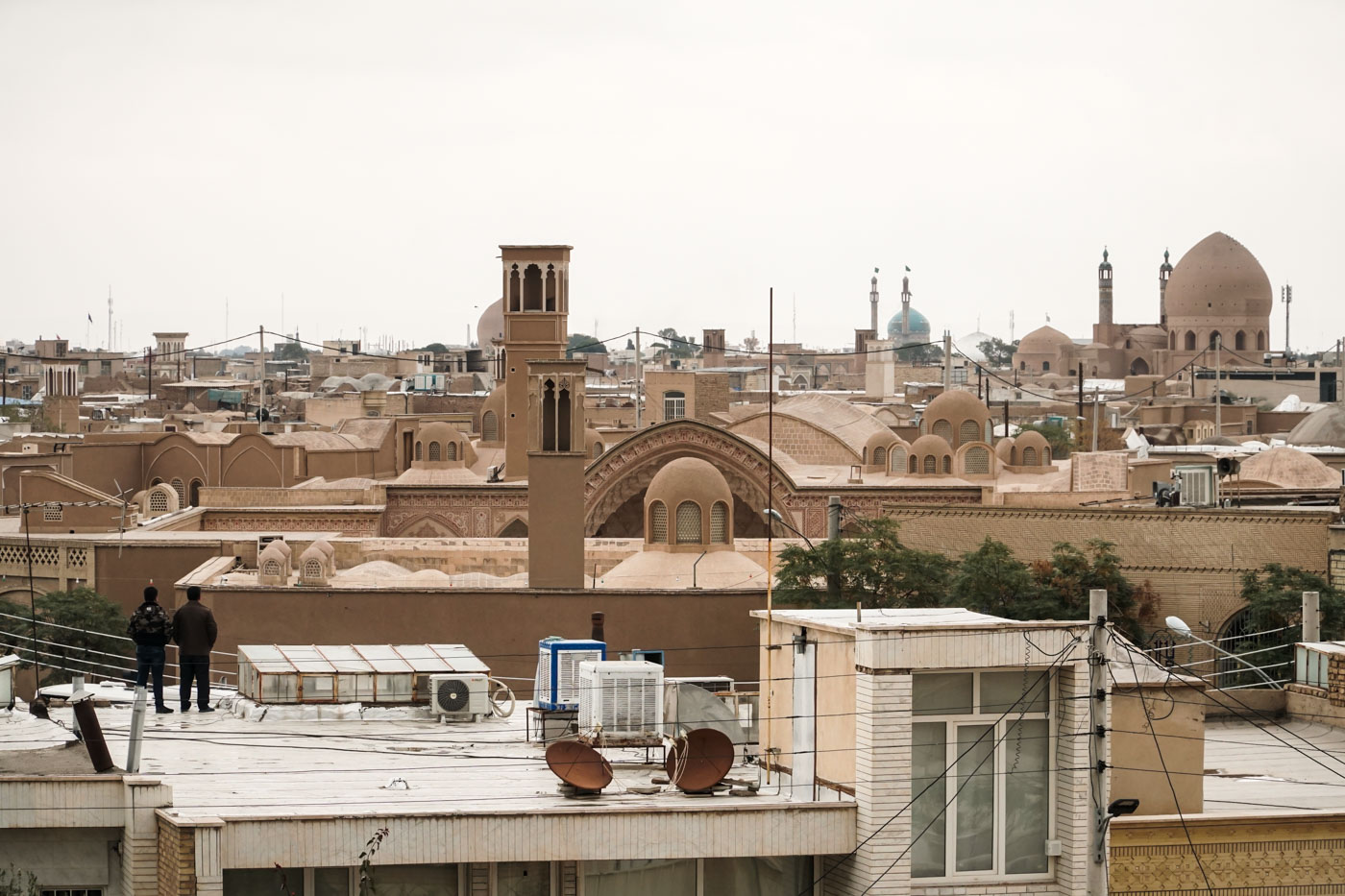 dois homens no teto de uma casa olhanda para a cidade de Kashan com mesquitas e torres ao fundo