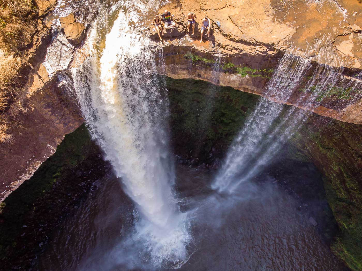 The Ezmeril Waterfall in Brazil from above with a group of people sitting in the edge of the fall the goes into a massive hole in the mountain