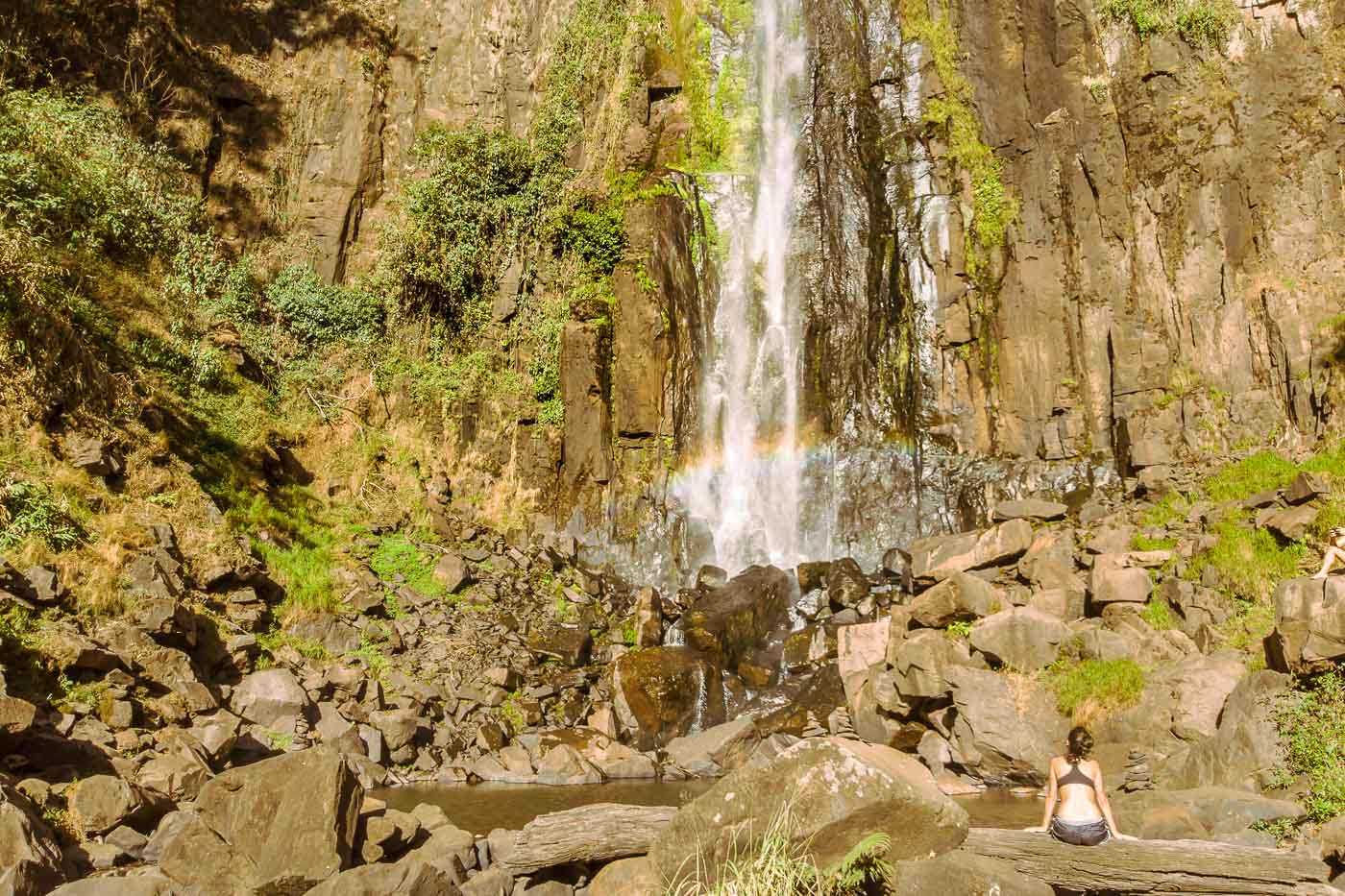 Fernanda sentada nas pedras em frente a cachoeira do Itambé