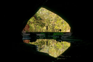 Dentro da caverna do Itambé com a Fê na entrada e refletindo na água que sai da caverna