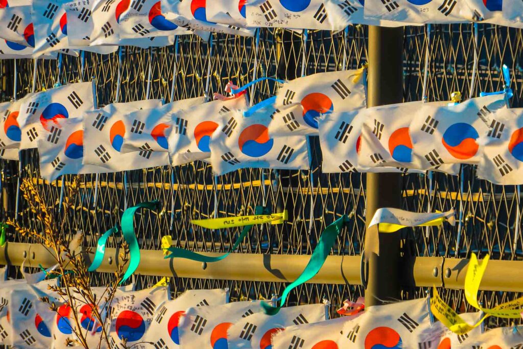 Many Korean flags attached to a barbed wire in the border between South and North Korea Muitas pequenas bandeiras da Coreia do Sul presas a uma grade de arame farpado na fronteira entre a Coreia do Sul e do Norte