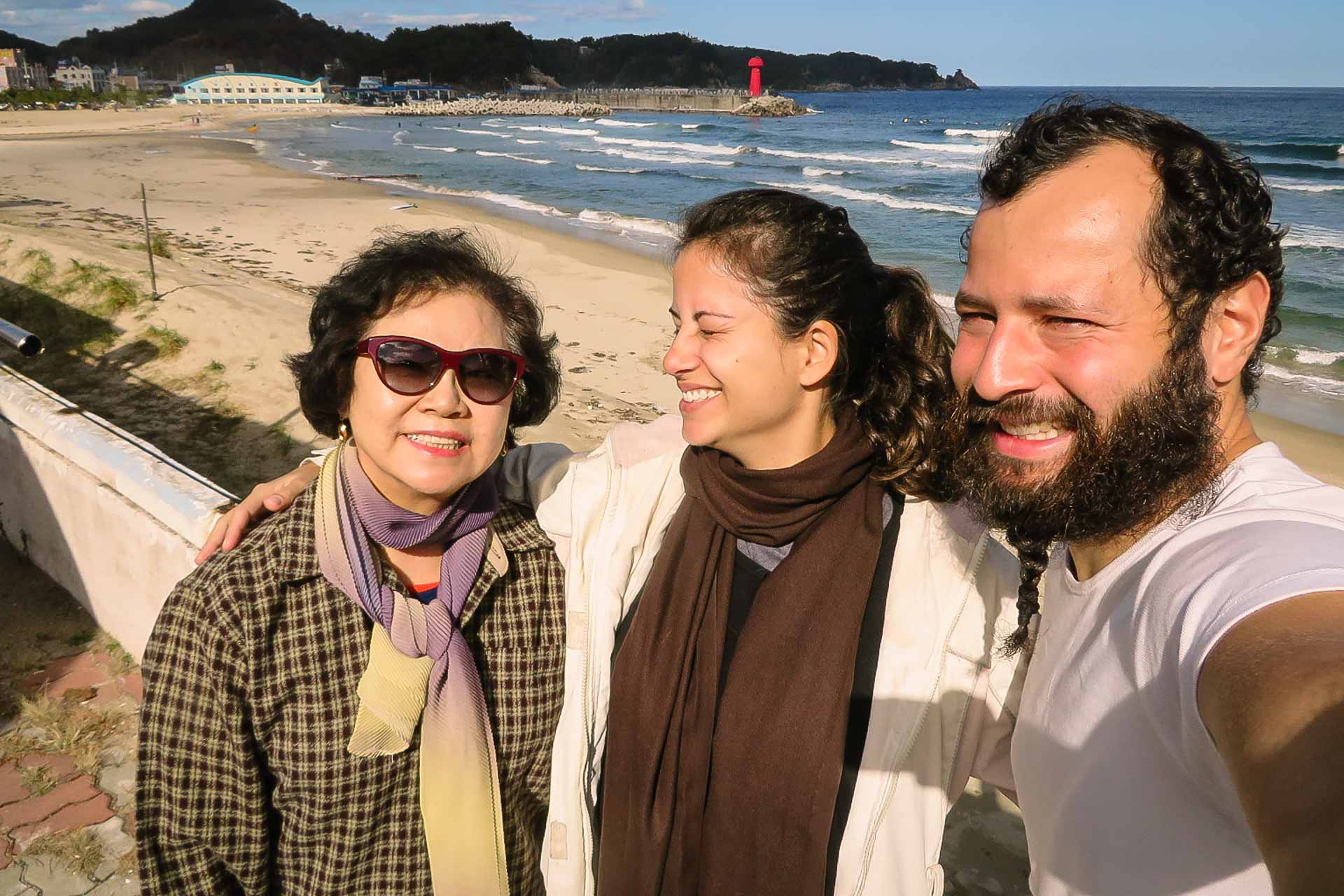 Um senhora coreana, Fernanda e Tiago na frente da praia da Coreia do Sul
