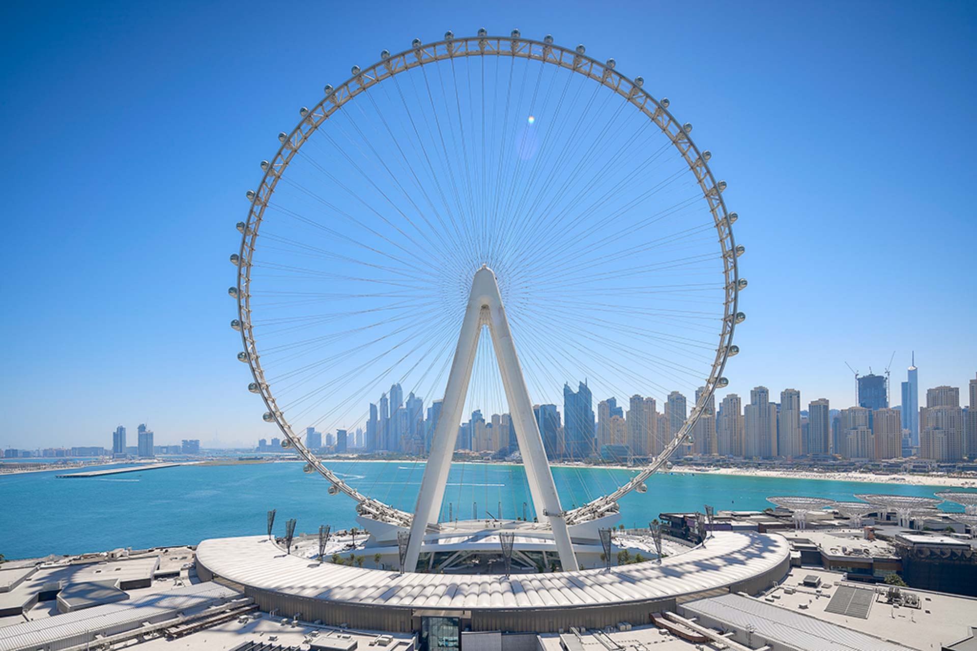 The massive Dubai ferris wheel and its large buildings in the background with a blue ski