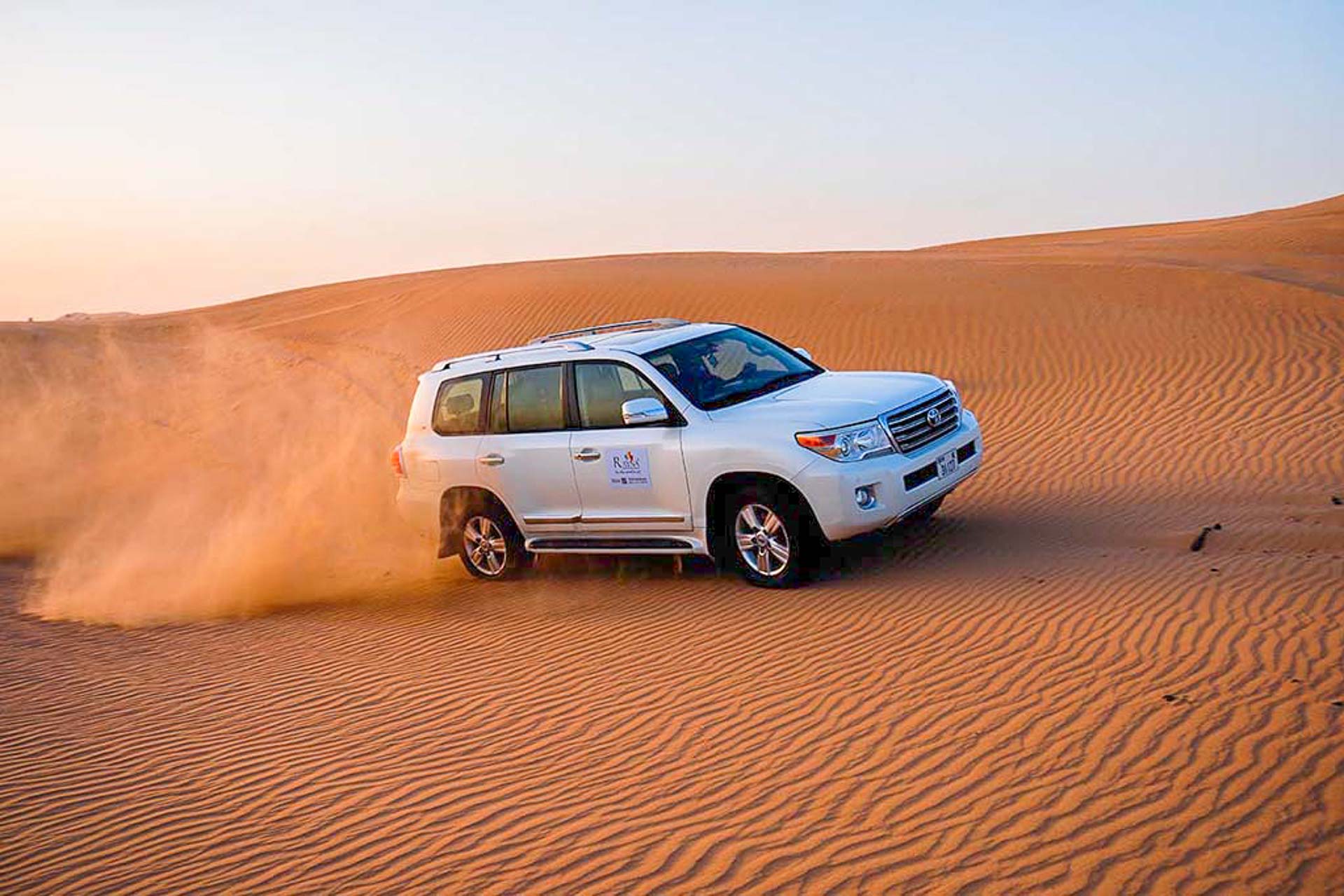 Car riding on desert sending sand up in the air