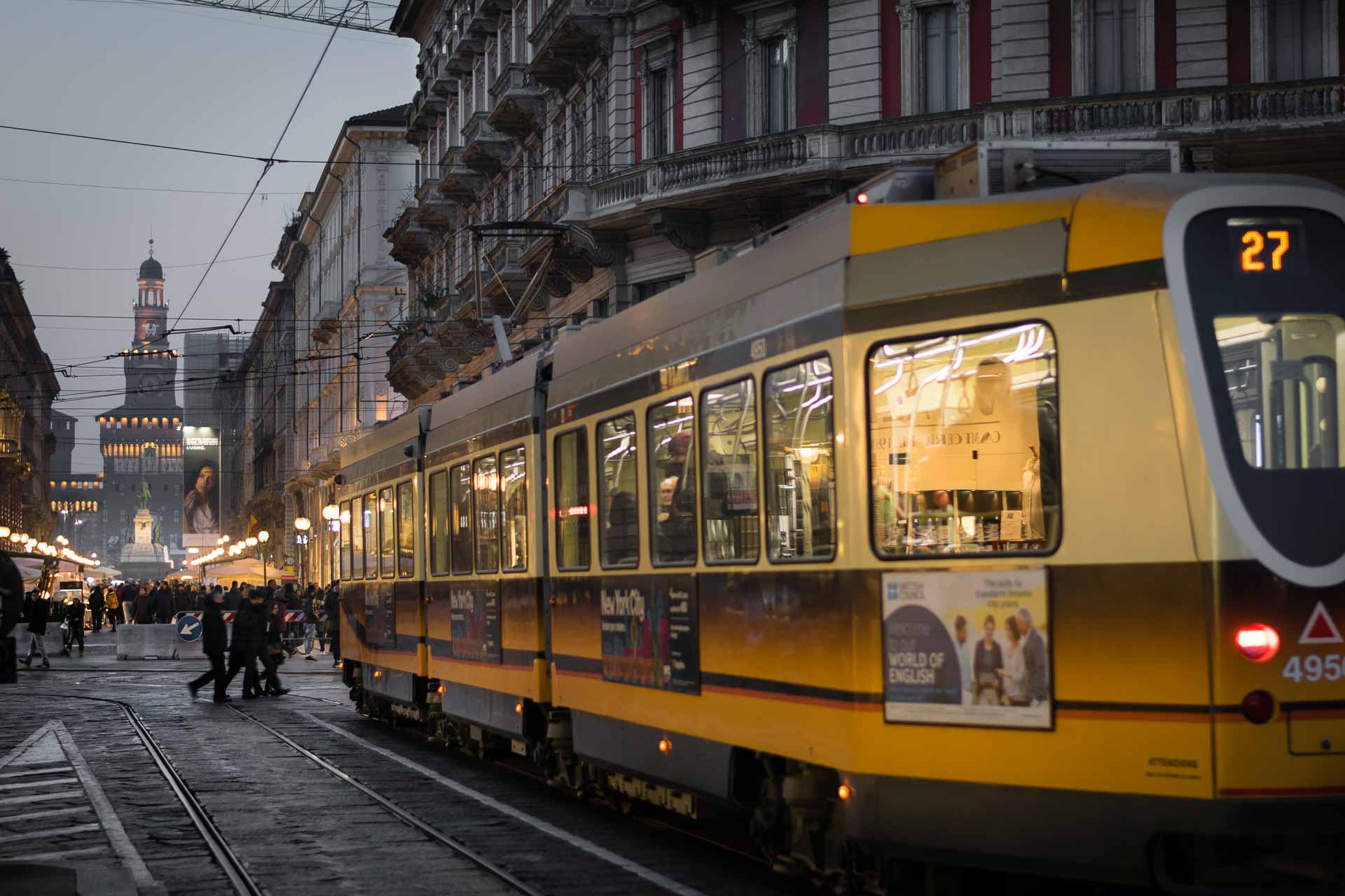 a tram crossing the city carrying people with a tower in the end of the road