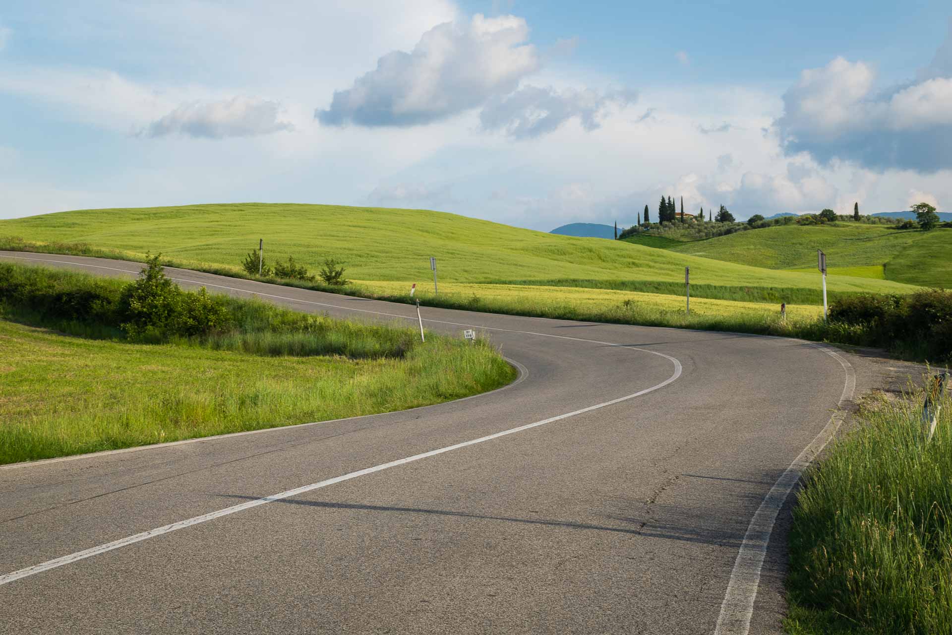 an empty road turning to left in the middle of a green field in an open sky in Tuscany town