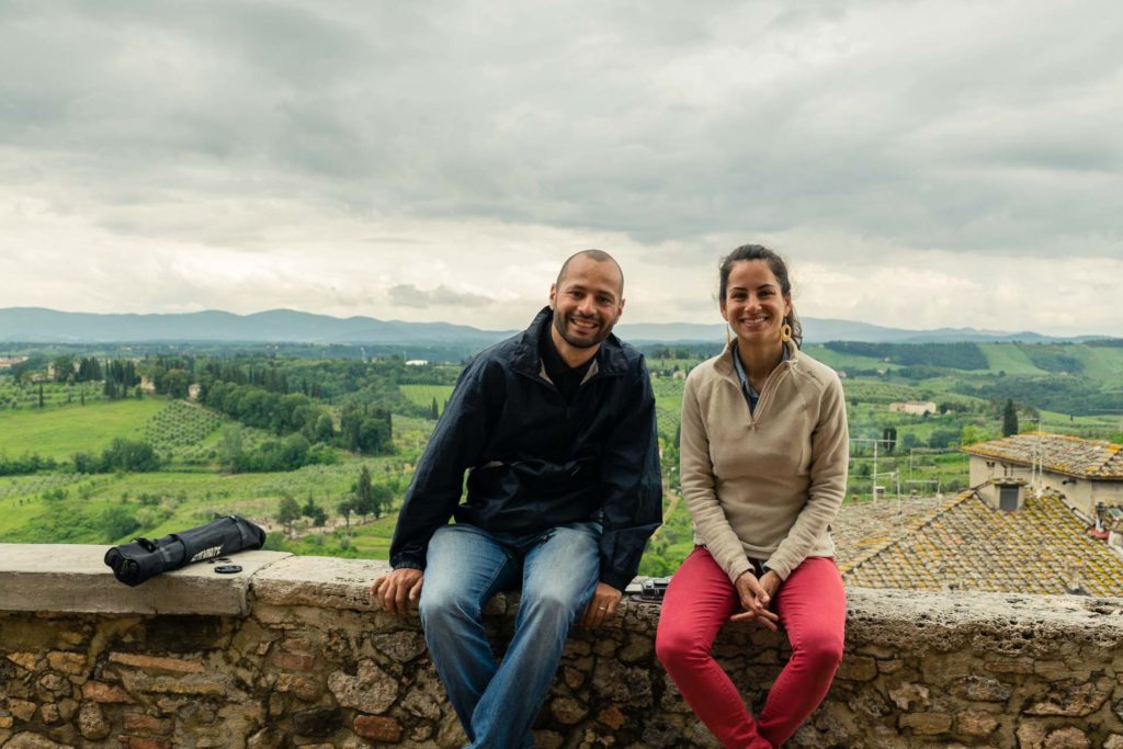 Tiago e Fernanda sentado no muro com um campo verde ao fundo