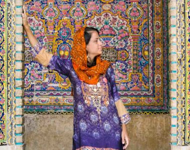 Fe with colourful clothes in front of a mosque with colourful tiles