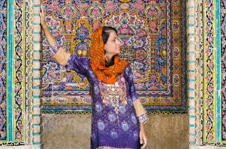 Fe with colourful clothes in front of a mosque with colourful tiles
