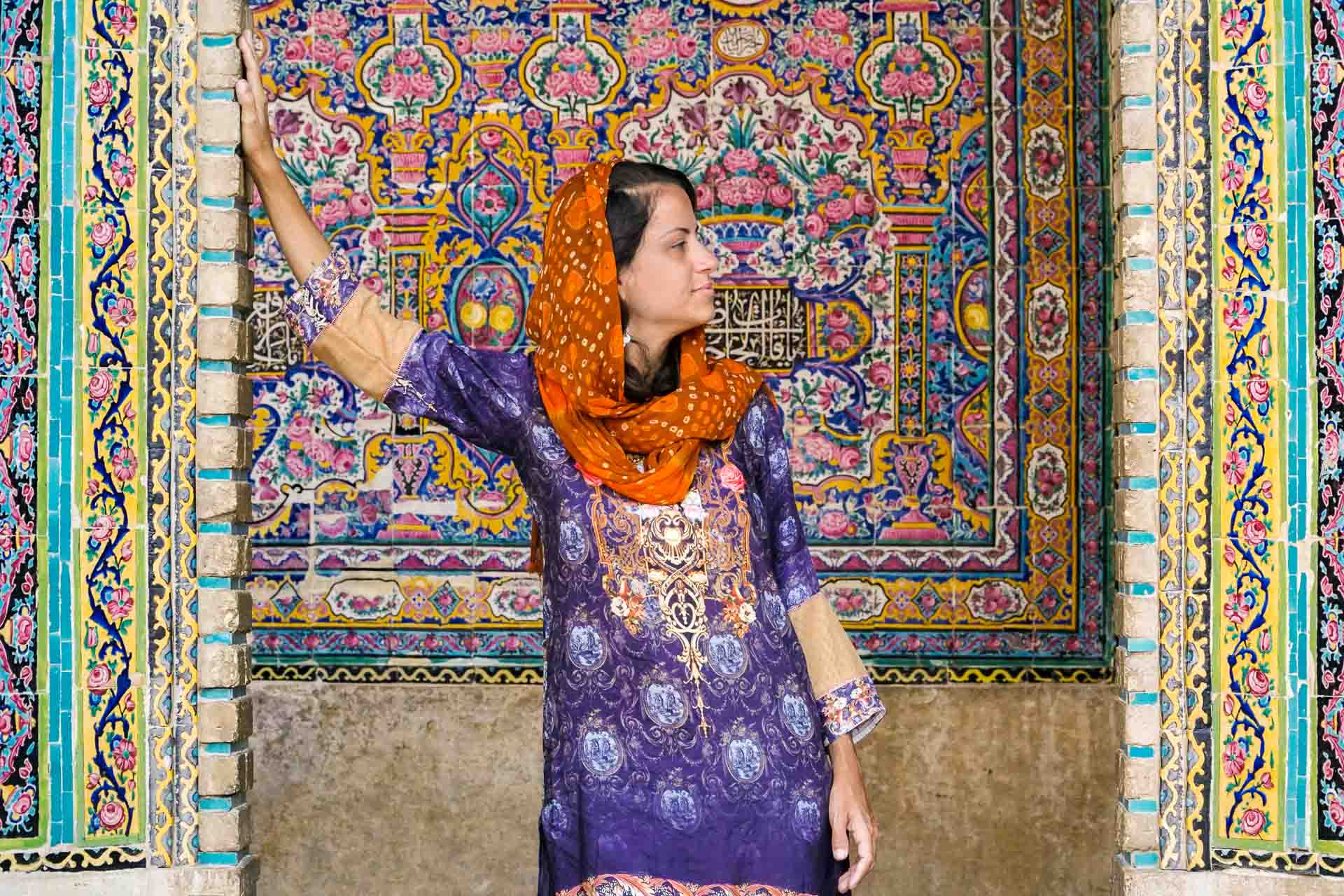 Fe em roupas coloridas em frente a mesquita de azuleijos coloridos