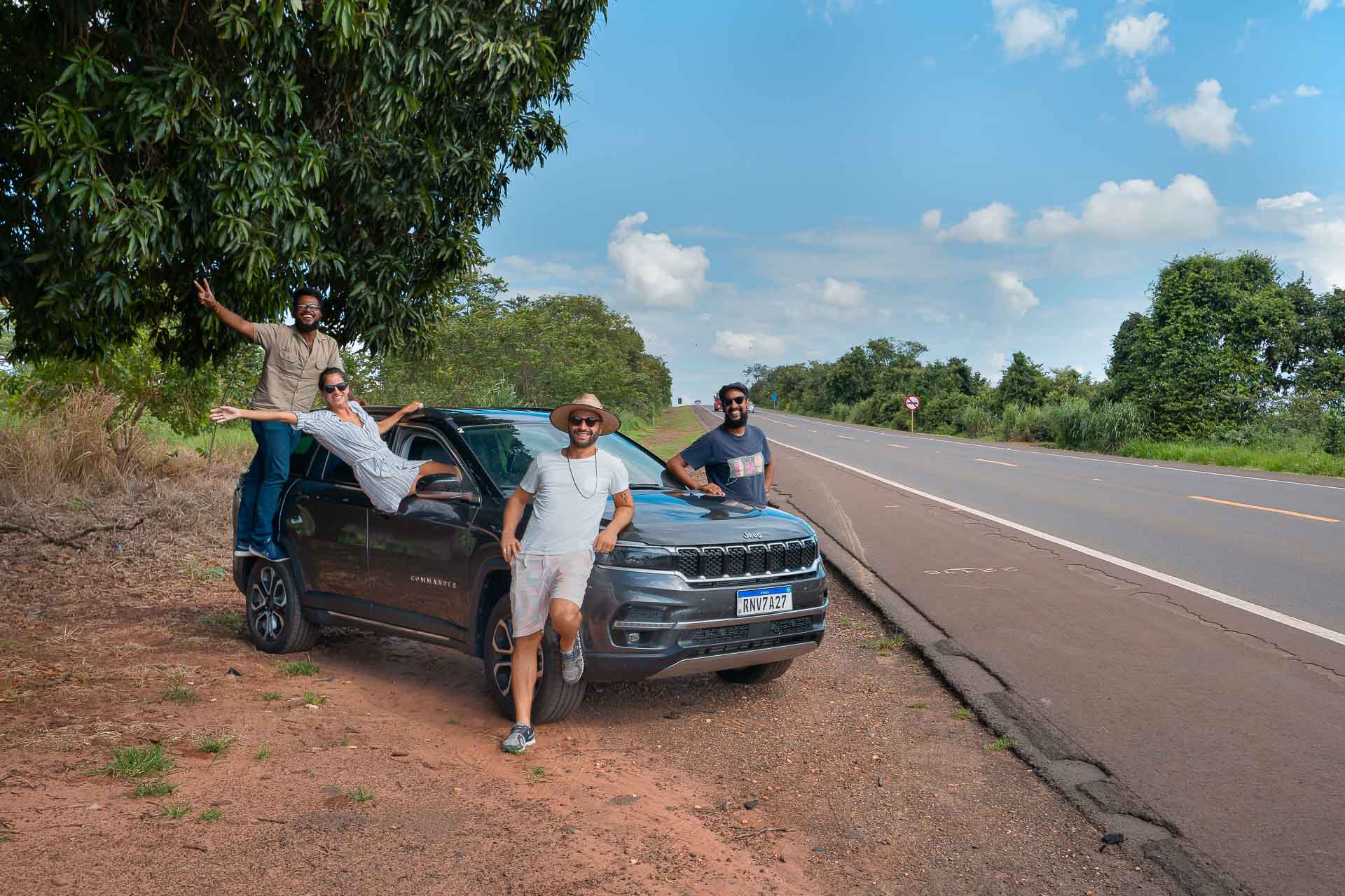 Carro parado no acostamento com Tiago e Fernanda e dois amigos posando na estrada