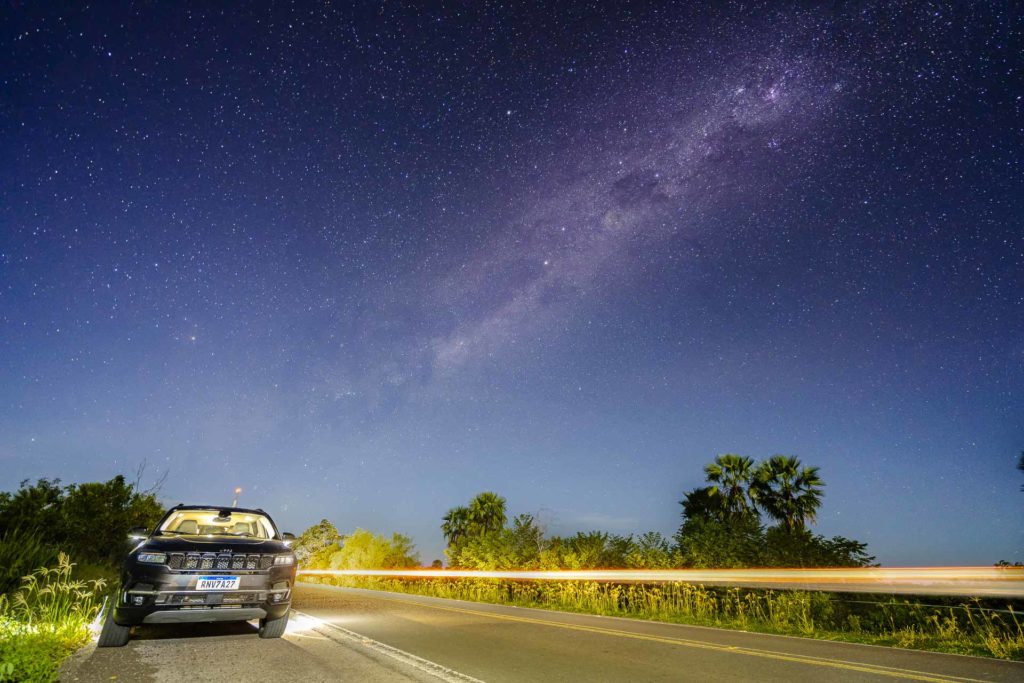 Um carro na beira da estrada a noite com a via láctea aparecendo no céu do Pantanal do Brasil