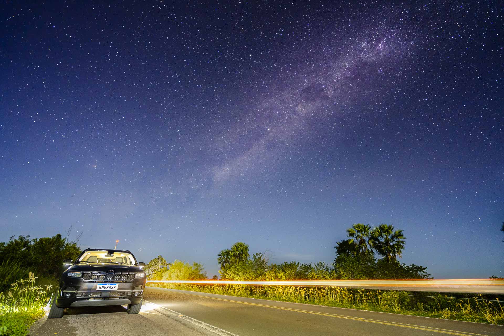 Carro parado no acostamento da estrada com a via láctea no céu