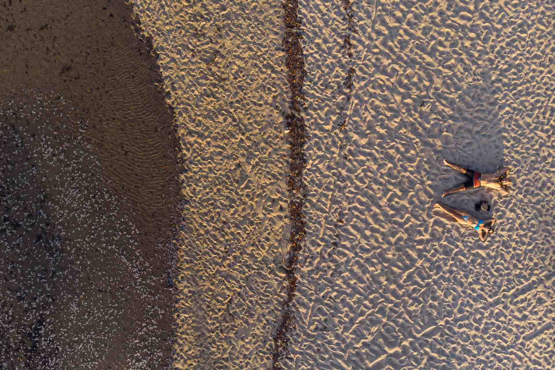 a 90 degrees view from above of Tiago and Fernanda laying down in the sand in Boipeba Brazil