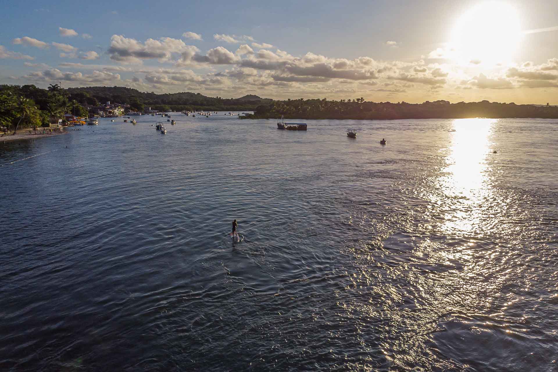 Vista aerea da praia da Boca da Barra com o por do sol na Bahia e uma pessoa fazendo stand-up paddle