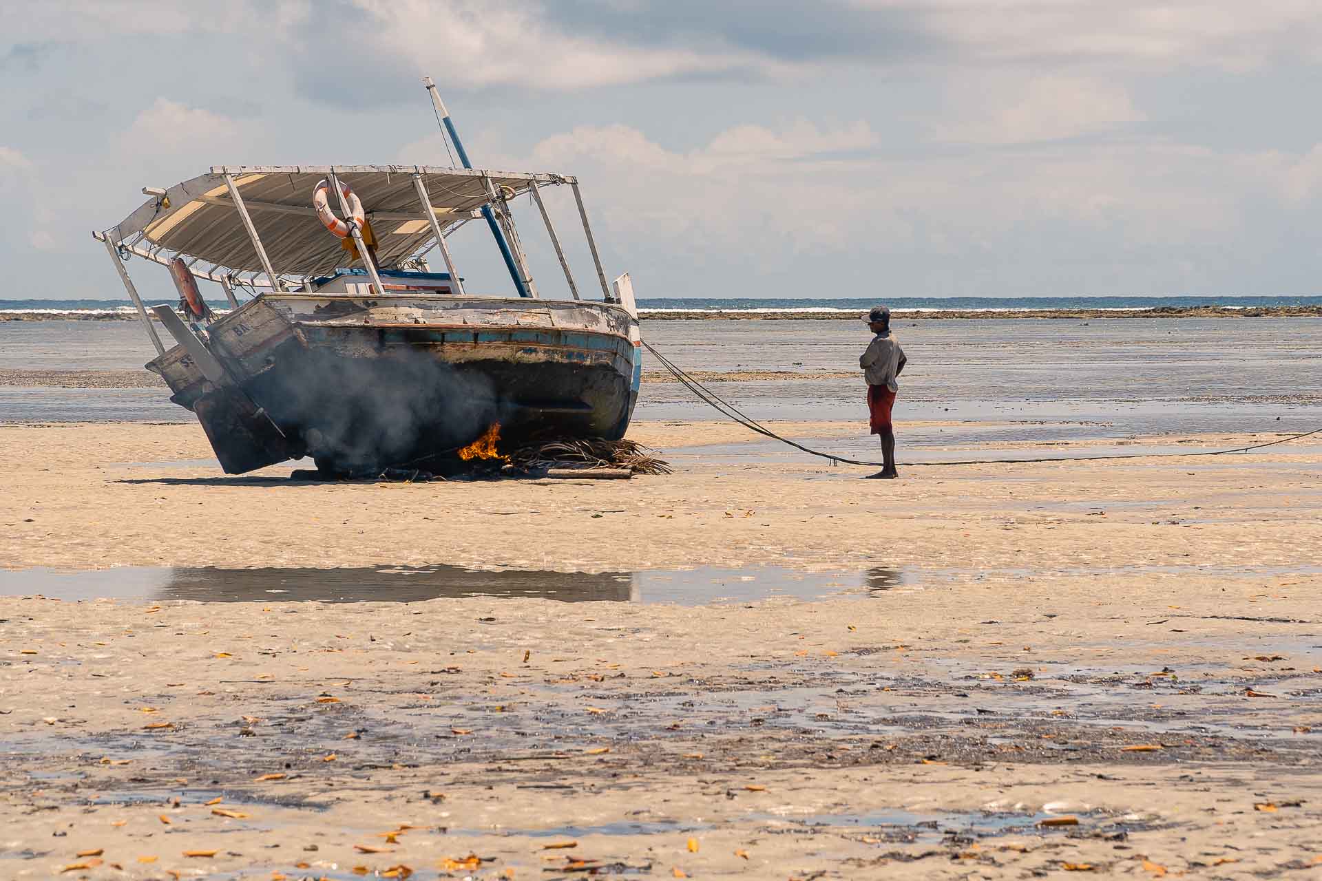 Um pescador colocando fogo embaixo do casco do barco para limpar de pragas em plena praia de Boipeba