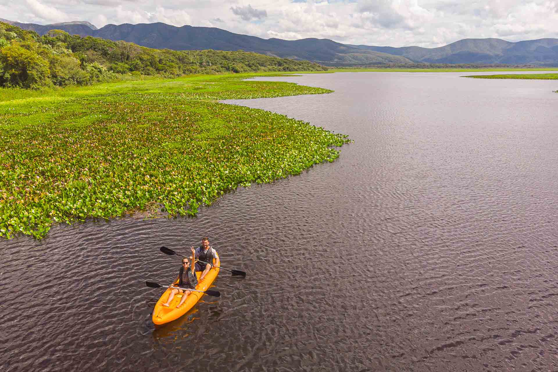 Duas pessoas em um kayak no rio com a serra do amolar ao fundo visto do alto