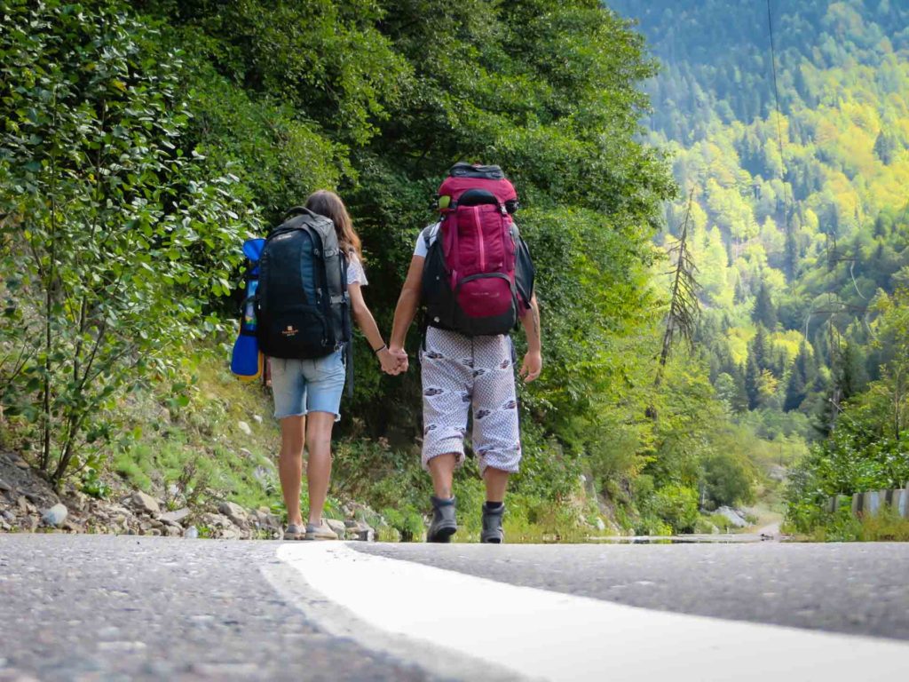 Tiago e Fernanda andando pela estrada da Georgia com as backpack nas costas e muita mata ao redor