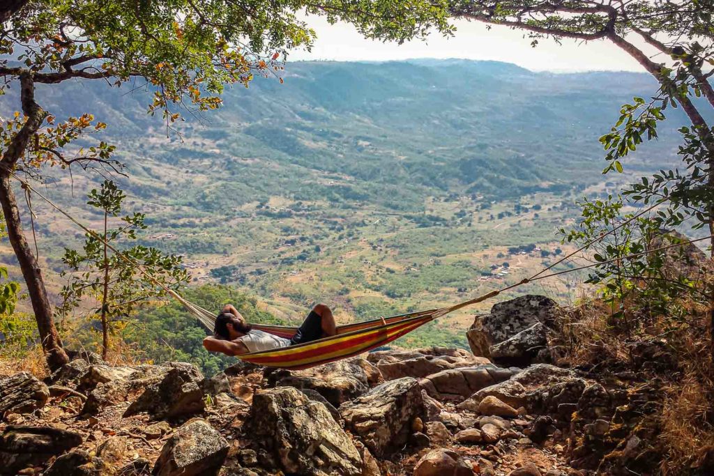 Tiago deitado na rede na beira de um precipício com uma vista para um vale e o mar ao fundo no Malawi