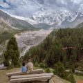 Tiago and Fernanda sitting on a bench looking at Nanga Parbat snowed peak mountain surrounded by a forest in Fairy Meadows