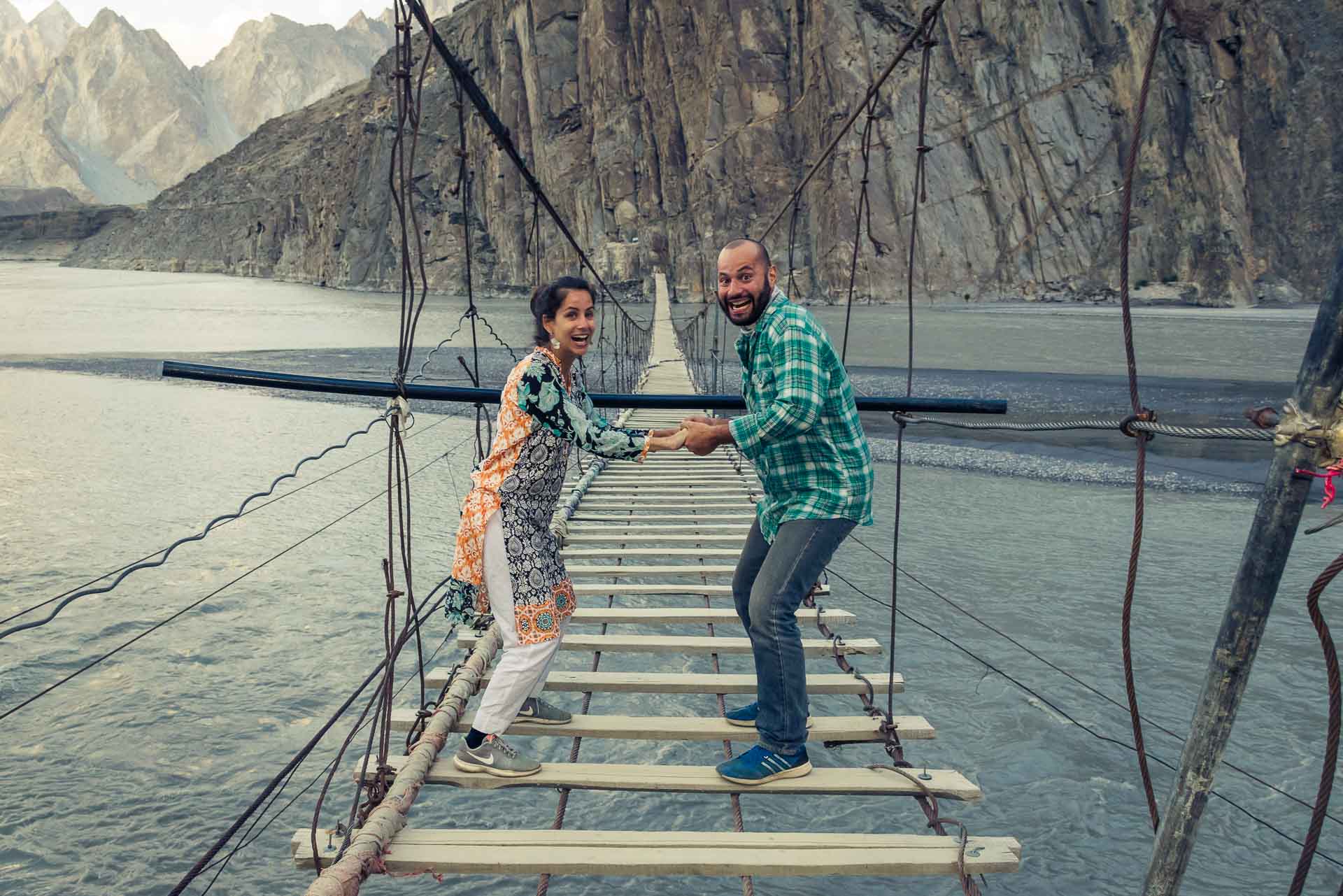 Tiago e Fernanda segurando as mãos no meio de uma ponte bem perigosa acima do rio no Paquistão