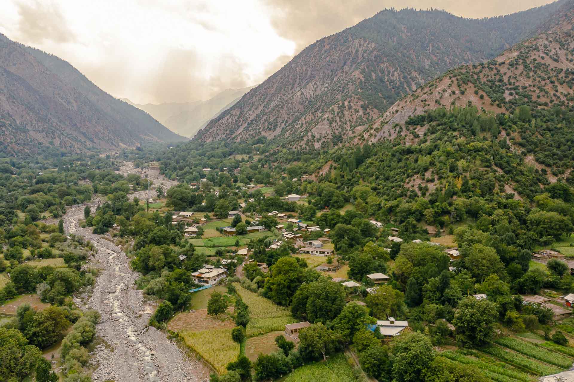 Aerial view of the Kalash Valley with the sun in between clouds and the dry river and the village