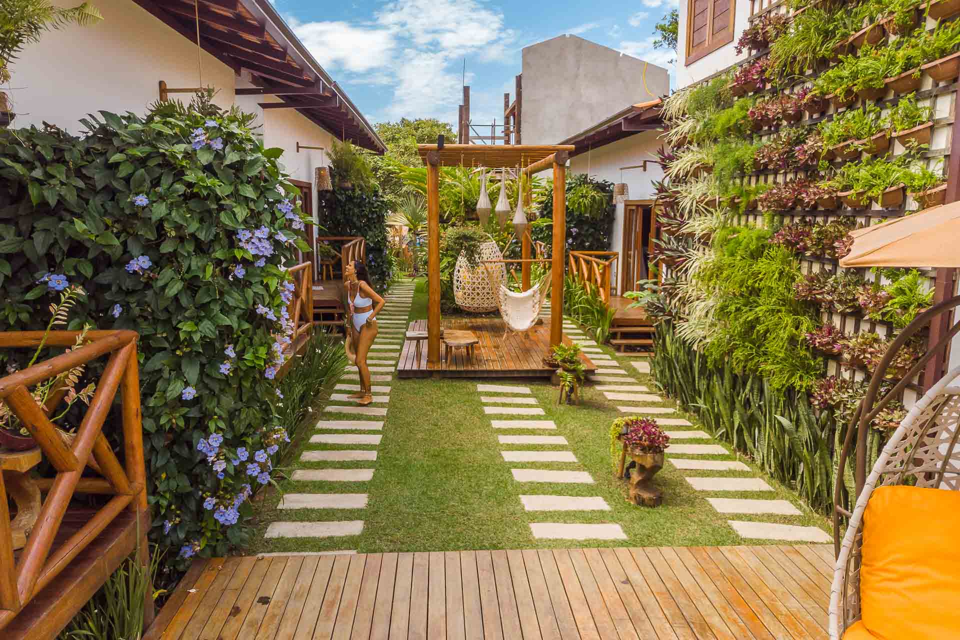 Dentro da pousada com um corredor cheio de plantas e aberto e os quartos ao lado