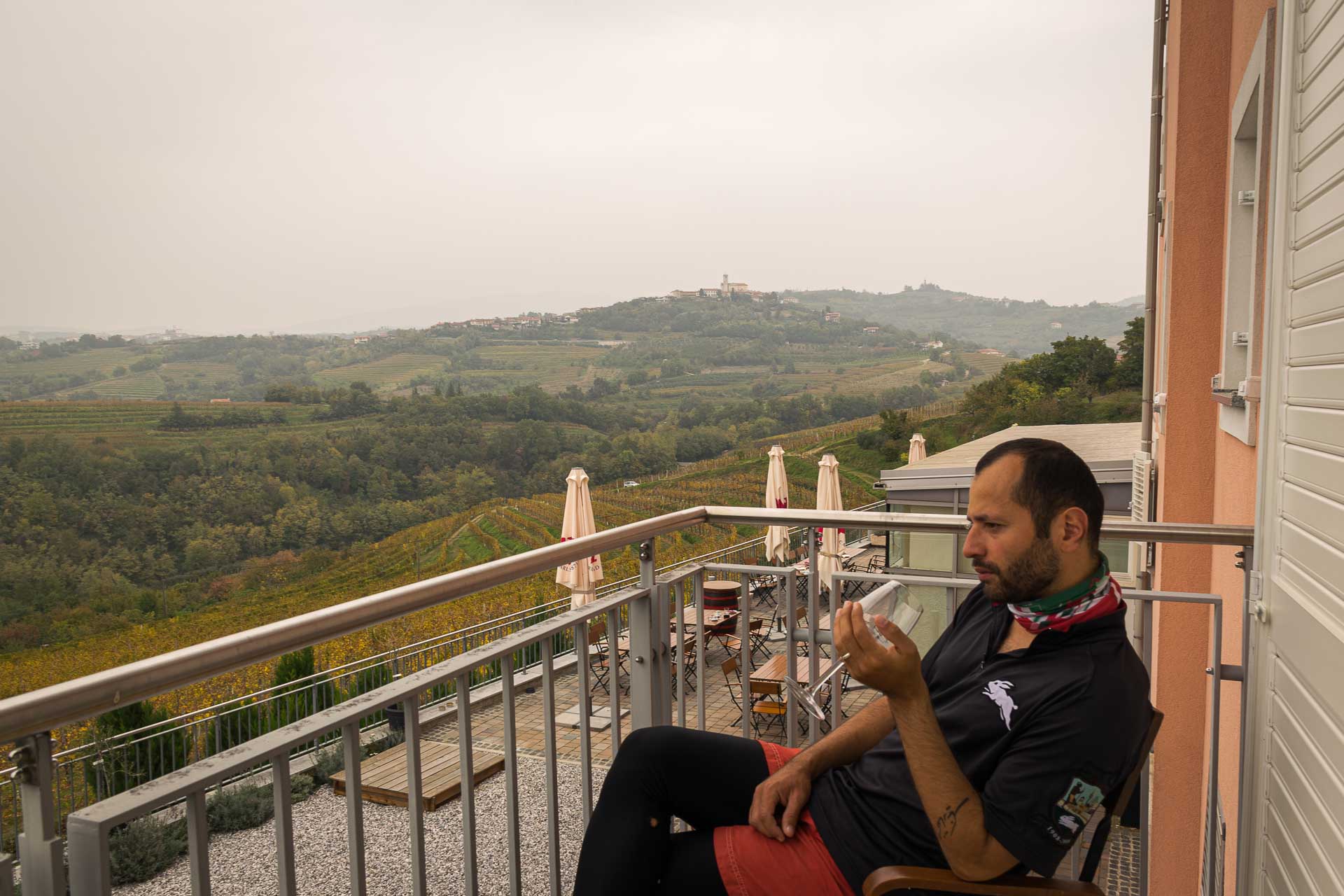 Tiago na varanda de um hotel na Eslovênia bebendo uma taça de vinho e observando a paisagem campestre