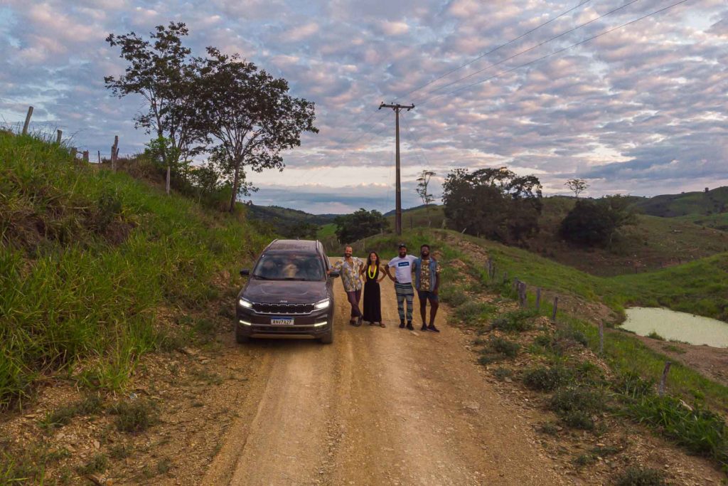 A car with a group of people posing in the middle of a dirty road