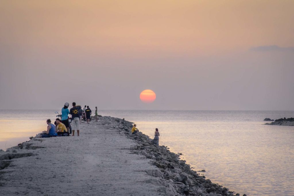 The sun setting in the horizon with a natural pier with people watching it