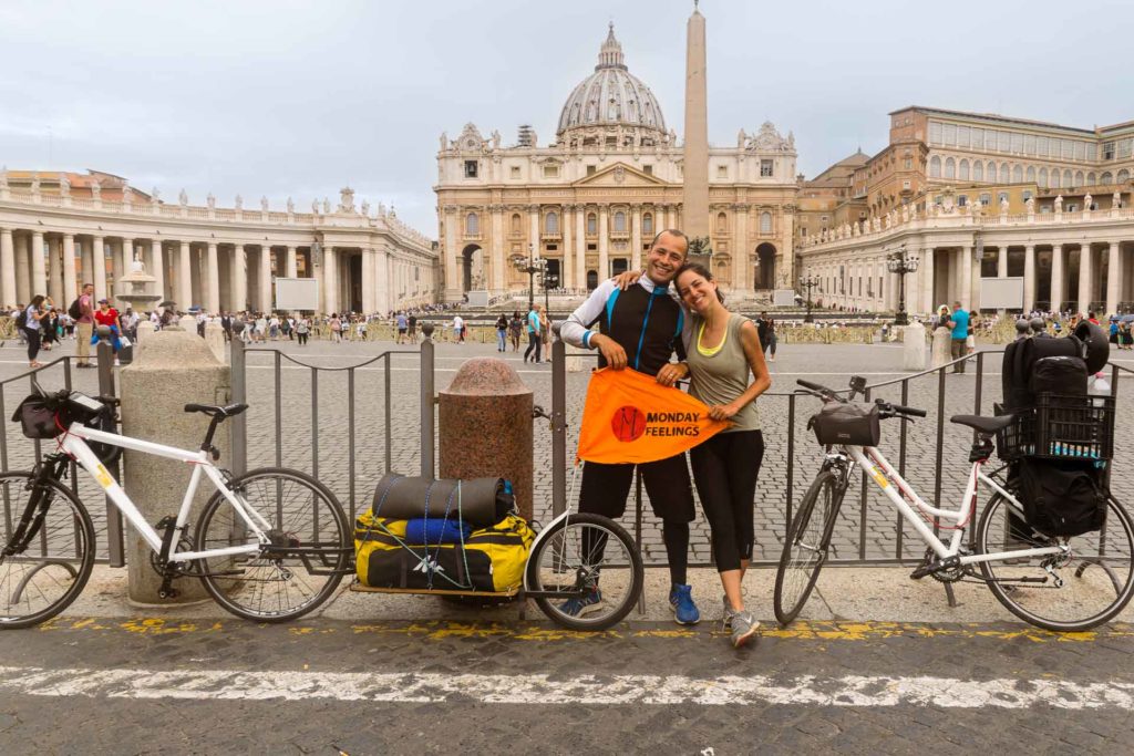 Tiago and Fernanda with their bikes in front of the Vatican with the Monday Feelings flag